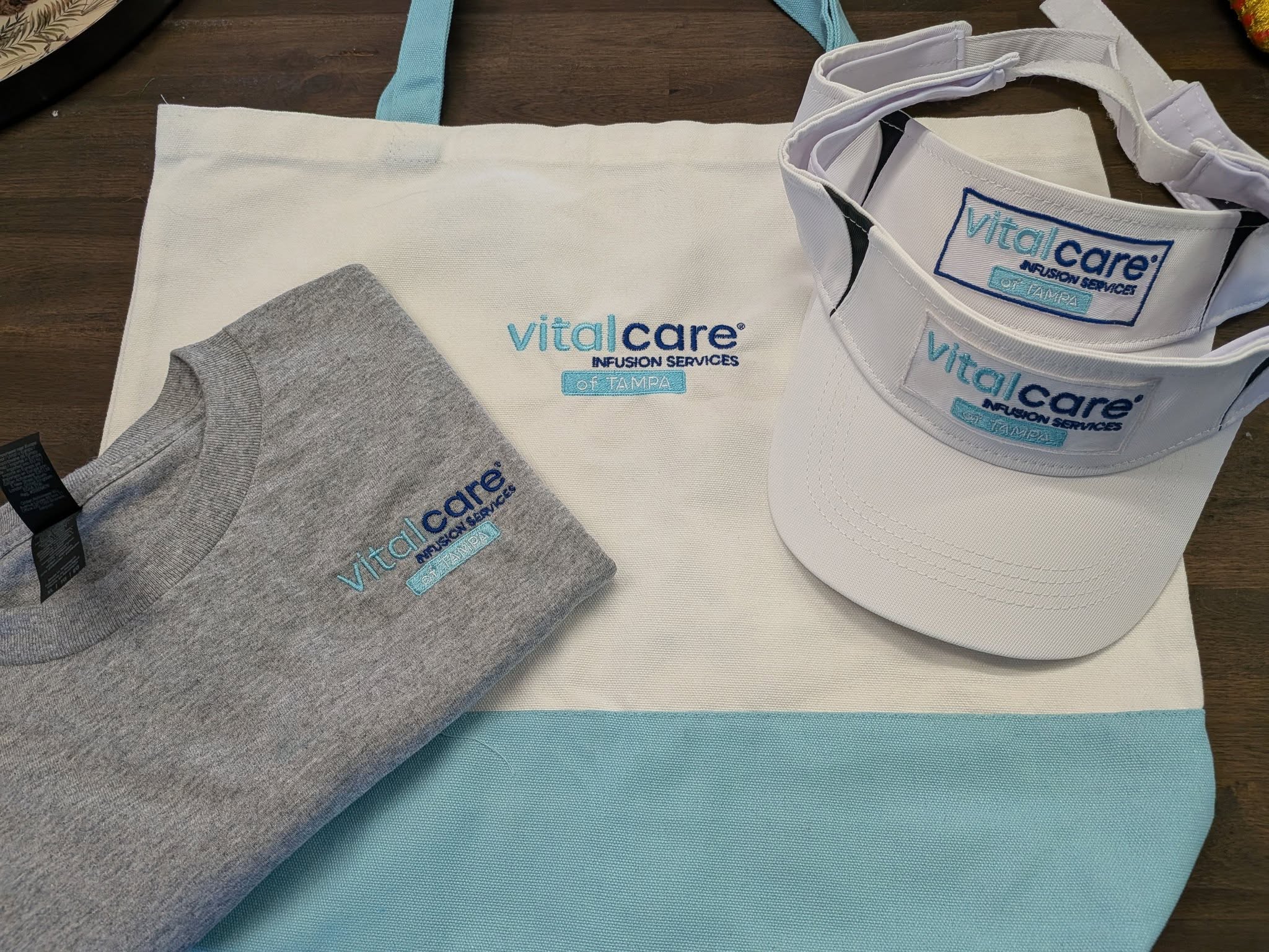 Vitalcare Infusion Services of Tampa branded kit — tote, tee, and visors with custom embroidery